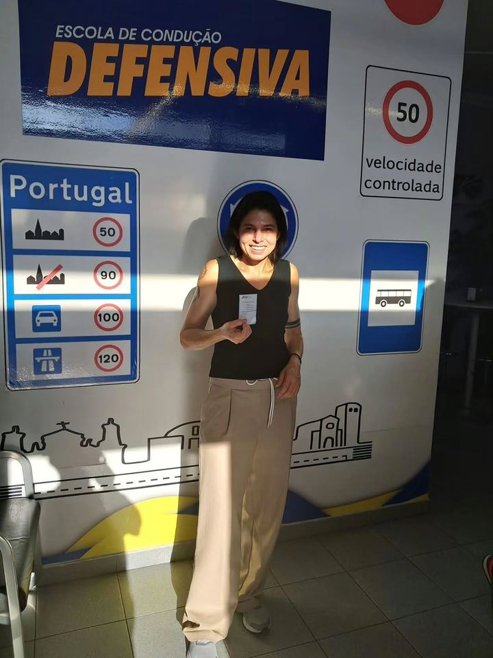 Nova condutora a mostrar a carta em frente à parede de sinais da escola